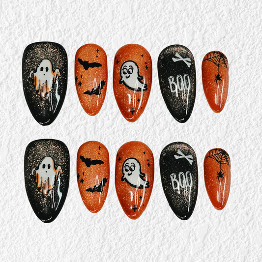 A set of ten Halloween-themed press-on nails arranged in two rows on a textured white background. The nails feature spooky designs including ghosts, owls, bats, 'BOO' text, spiderwebs, and a tree on black glittery almond-shaped nails and orange glittery oval nails.