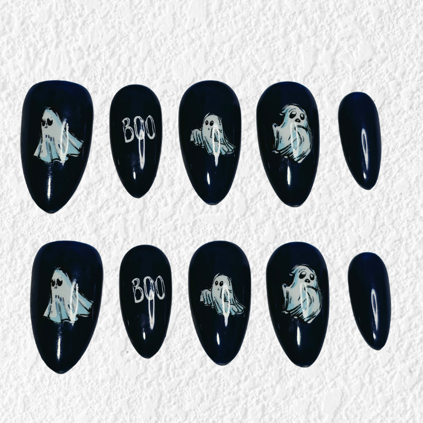A set of ten black press-on nails arranged in two rows on a textured white background. Five nails feature white ghost illustrations, two feature the word 'BOO' in white, and two are plain black.